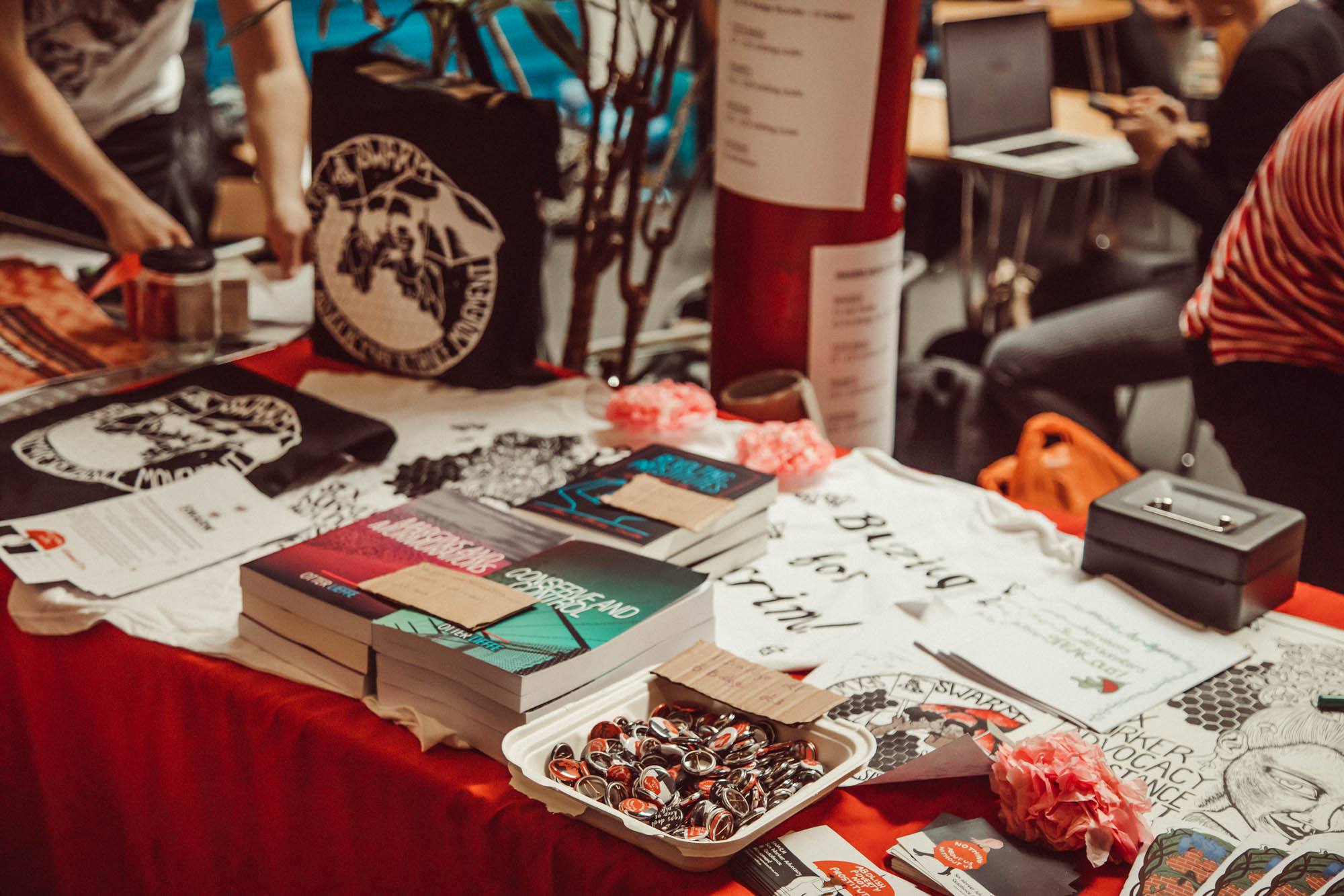 A table featuring various merchandise from SWARM conference, including pints, badges, books and tshirts.