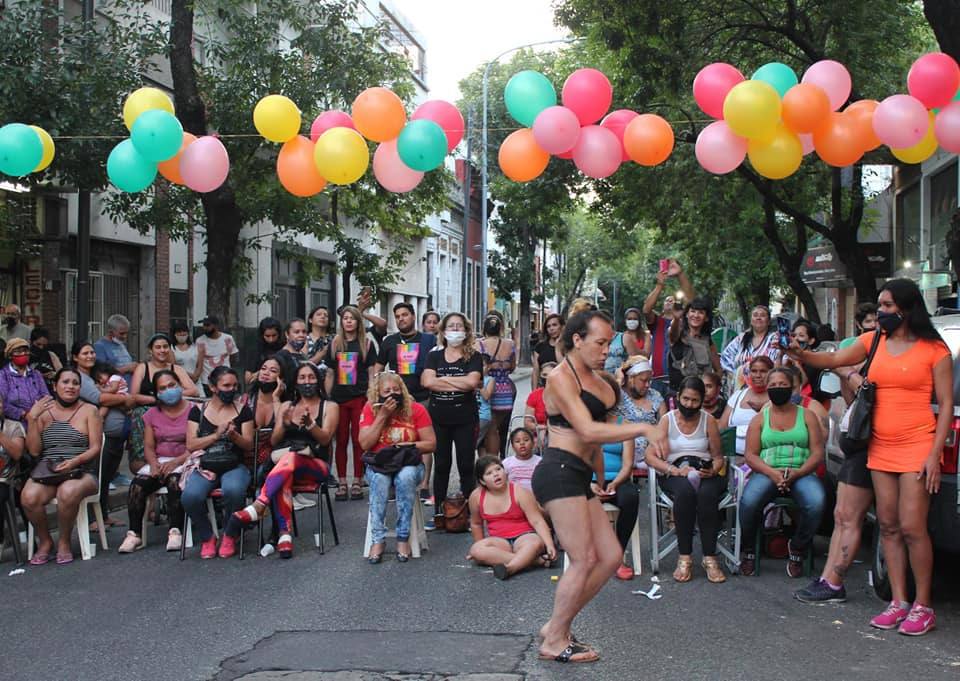 A white performer in black shorts and a black bra dances at a sex worker street party in Buenos Aires. A large crowd is gathered around them, with multi-coloured balloons.
